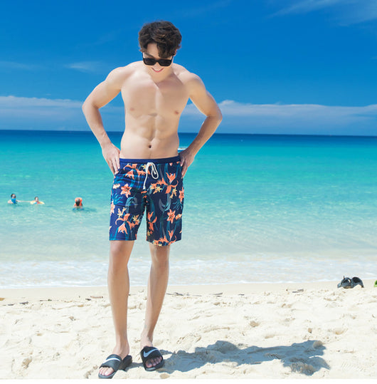 Man wearing navy blue swim shorts with a vibrant orange and green floral pattern, standing on a sunny beach. - Image 9