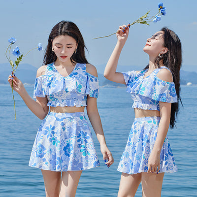 Two women in matching blue and white floral print swimsuits with off-shoulder ruffled tops and A-line skirts by the ocean. - Image 12