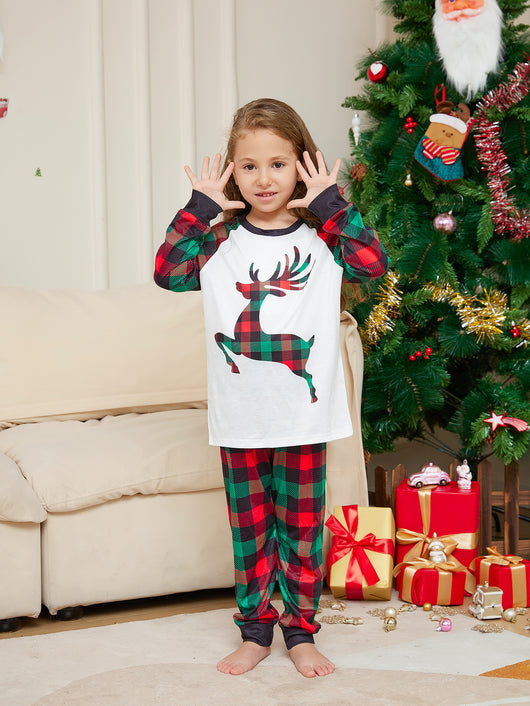 Two children in matching red and green plaid Christmas pajamas with a reindeer graphic, standing by a Christmas tree. - Image 6
