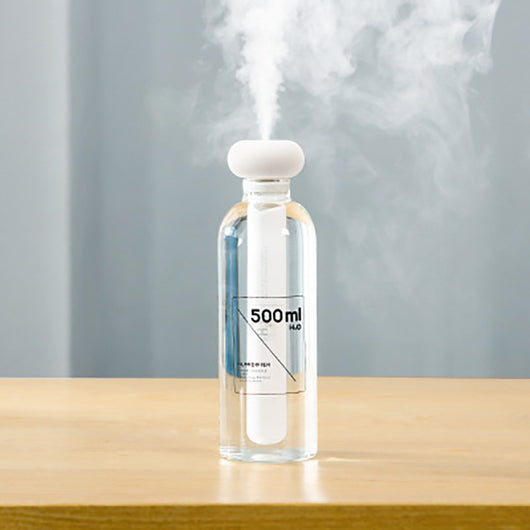 Clear bottle-shaped USB humidifier with a white donut-style top, emitting a stream of cool mist on a wooden table. - Image 8
