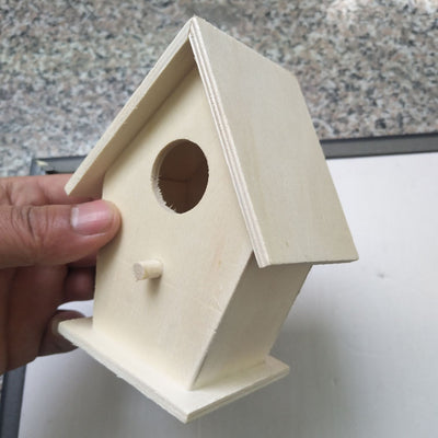 Unfinished wooden birdhouse with a circular entrance hole and a small perch, held by a hand. - Image 3