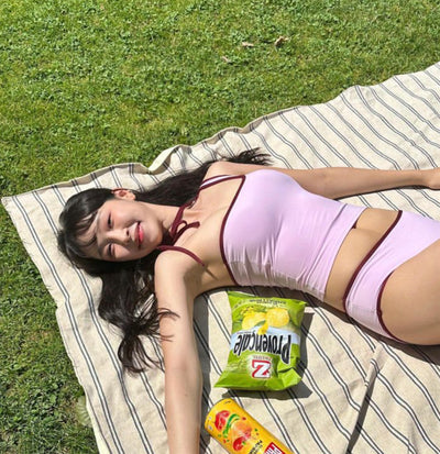 Women's light purple one-shoulder swimsuit with dark red contrast trim, lying on a striped blanket on green grass. - Image 7