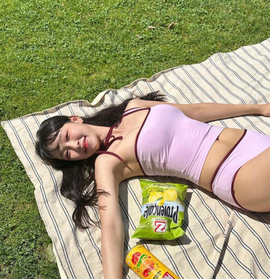 Women's light purple one-shoulder swimsuit with dark red contrast trim, lying on a striped blanket on green grass. - Image 7