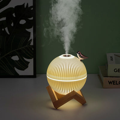 White spherical humidifier with ribbed texture, warm glow, metallic bird accent, and light brown wooden stand. - Image 6