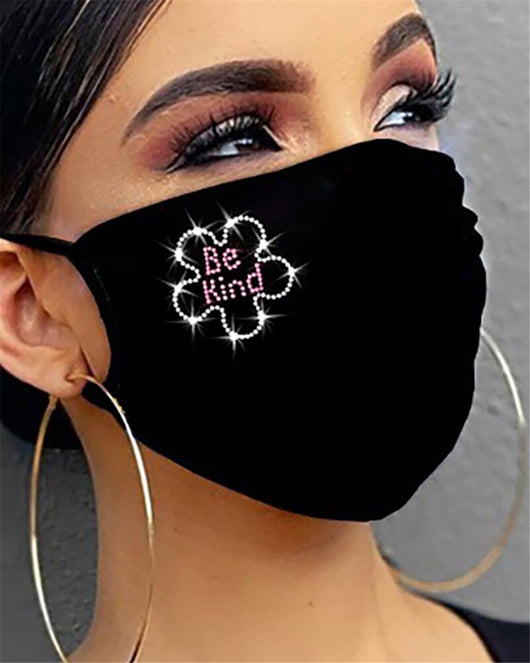 Black cotton face mask with a rhinestone flower design and "Be Kind" in pink rhinestones, worn by a person.