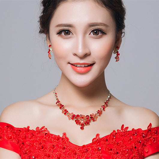 Red rhinestone bridal jewelry set featuring a floral necklace and matching dangle earrings on a model.