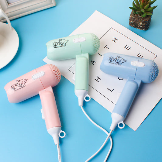 Light blue foldable hair dryer with a cartoon pig design, white power switch, and hanging loop.