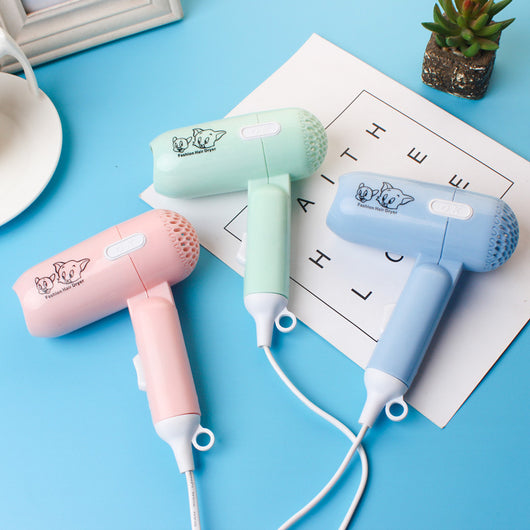 Light blue foldable hair dryer with a cartoon pig design, white power switch, and hanging loop.
