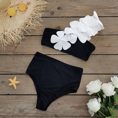Women's black one-shoulder two-piece swimsuit with large white floral appliques and high-waisted bottoms.