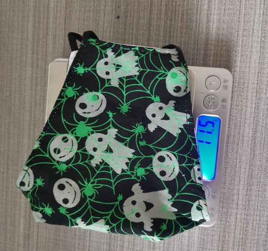 Black cloth face mask with white Halloween witch, bats, and jack-o'-lantern pattern, shown glowing green in the dark. - Image 9