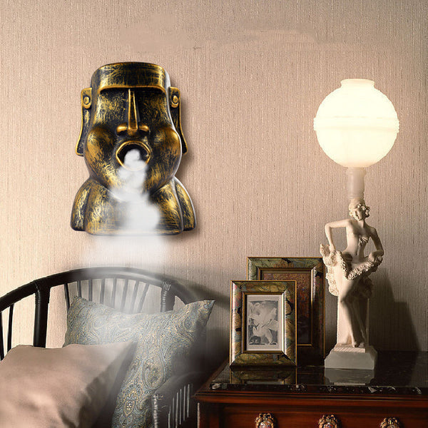 Retro gold and black stone portrait humidifier ornament emitting mist, mounted on a textured wall.