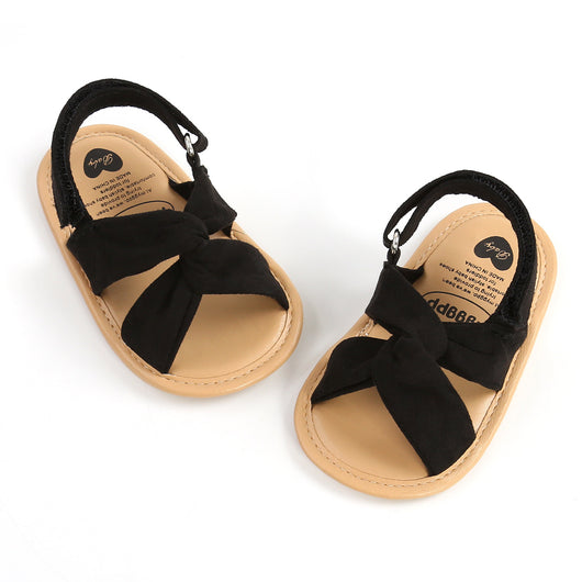 Black baby sandals with knotted cross straps and a matching black floral headband on a white background. - Image 37