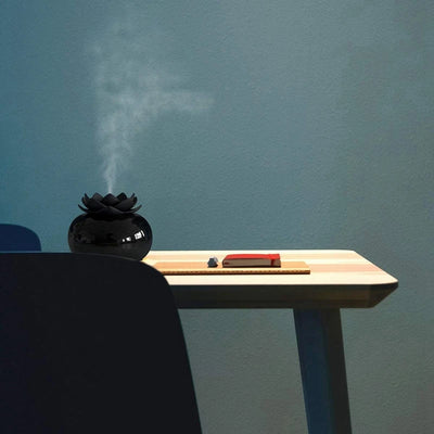 Black spherical aromatherapy humidifier with a lotus flower top, emitting mist, sitting on a gold decorative doily. - Image 8