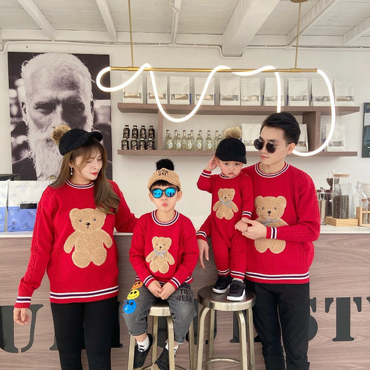 Family of three wearing matching red cable-knit sweaters with a brown teddy bear appliqué and striped trim. - Image 8