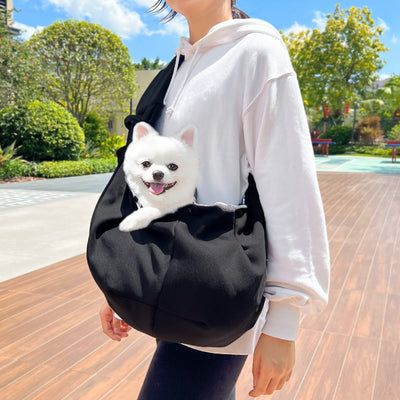 Person in white hoodie carrying a happy white dog in a navy blue pet sling bag outdoors. - Image 43