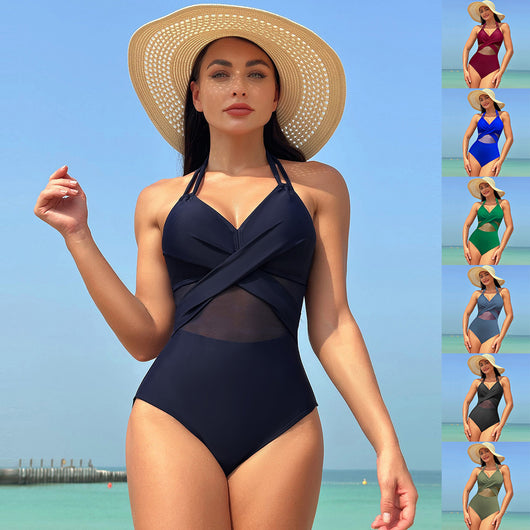 Woman in a green halter-neck one-piece swimsuit with cross-strap design and mesh cutouts, on a beach.