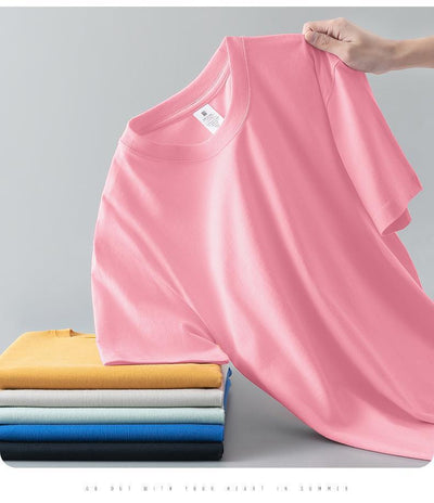 Light gray short-sleeve t-shirt with a round neck, held up to show its smooth fabric. A stack of folded t-shirts in various colors is visible in the background. - Image 16