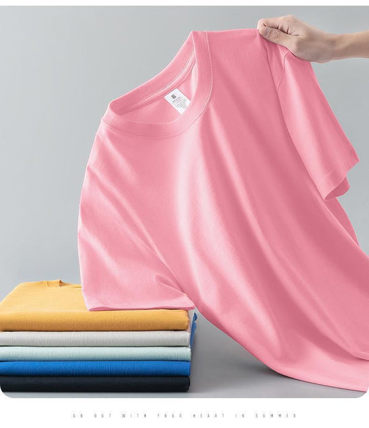 Light gray short-sleeve t-shirt with a round neck, held up to show its smooth fabric. A stack of folded t-shirts in various colors is visible in the background. - Image 16