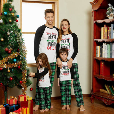 Family of four in matching Christmas pajamas with 'Dear Santa THEY'RE the NAUGHTY ones' graphic and green plaid pants.