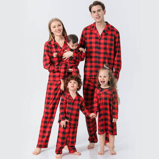 Baby in a red and black buffalo plaid long-sleeve pajama romper, viewed from the back with arms raised.