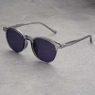 Fashionable round-frame sunglasses with transparent gray frames and dark gray lenses on a gray surface. - Image 10