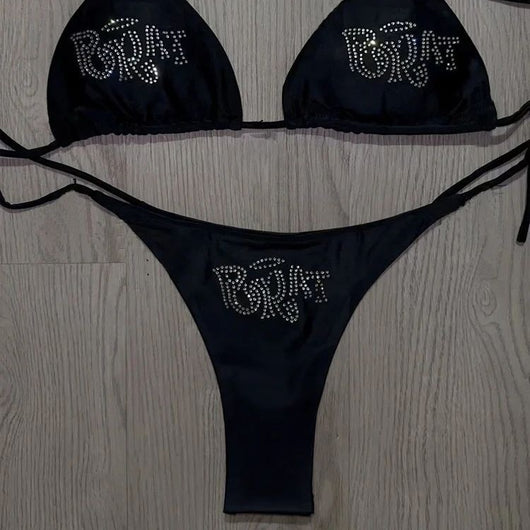 Black halter bikini with rhinestone 'BRAT' lettering on triangle top and tie-side bottom, displayed on white faux fur. - Image 2