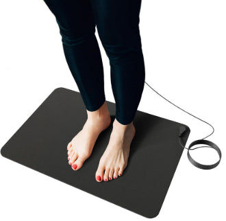 Person standing barefoot on a black rectangular grounding mat with a connected wire, used for earthing. - Image 5