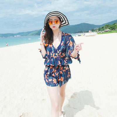Man wearing navy blue swim shorts with a vibrant orange and green floral pattern, standing on a sunny beach. - Image 6