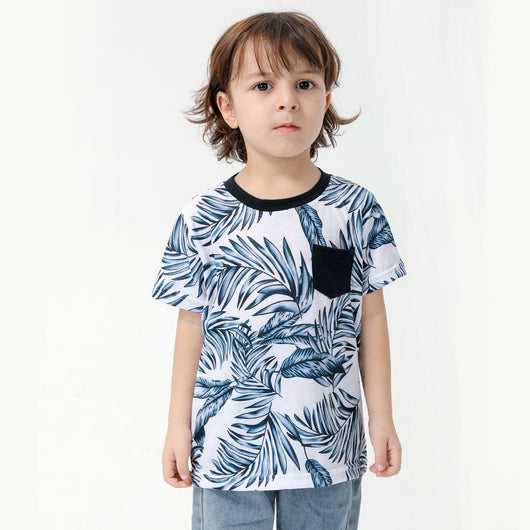 Young boy wearing a white short-sleeve t-shirt with blue tropical leaf print and a black chest pocket. - Image 6