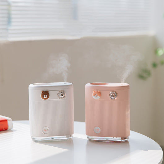 White cylindrical humidifier with ribbed texture, clear base, brown bear button, and silver dial, emitting mist on a white table. - Image 11
