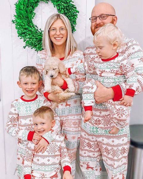 Family of four wearing matching green Christmas pajamas with white snowflakes and trees, red trim, sitting on a bed. - Image 2