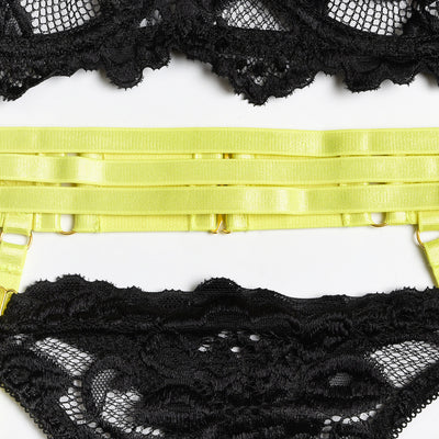 Woman in a neon yellow strappy harness lingerie set over a black lace bra and thong, sitting on a white bed. - Image 10