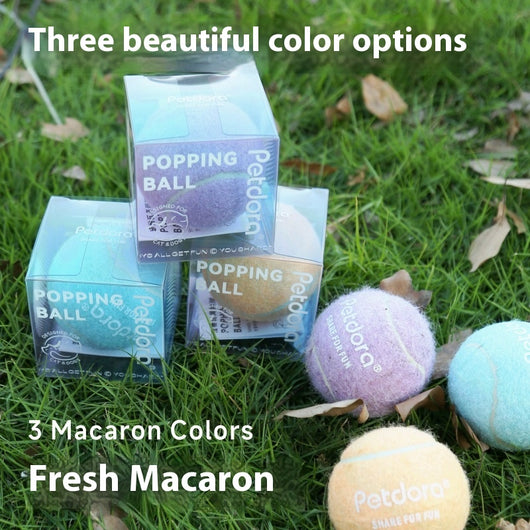 Peach yellow Petdora high elastic tennis ball dog toy next to its clear iridescent 'Popping Ball' packaging.
