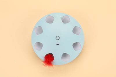 Light blue circular cat teaser toy with multiple cutouts and a red feather extending from one opening. - Image 6