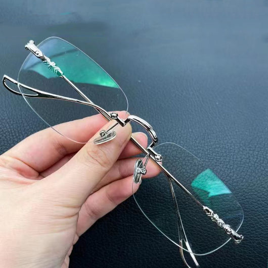 Silver rimless reading glasses with clear lenses held by a hand, featuring decorative temples and smart zoom technology.