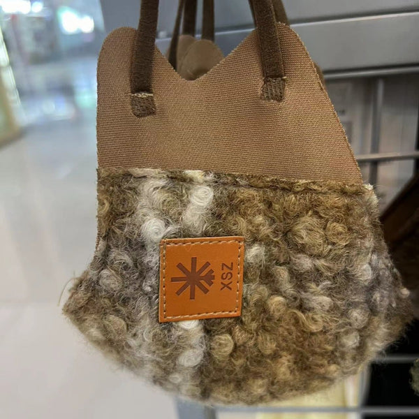 Beige curly plush warm mask with cream trim and a brown faux leather patch, held by a hand.