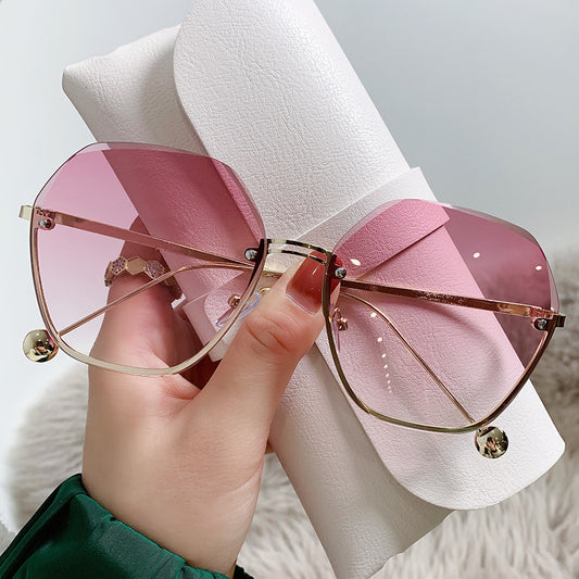 Elegant fashion sunglasses with gold metal frames and pink gradient lenses, held against a white case. - Image 2