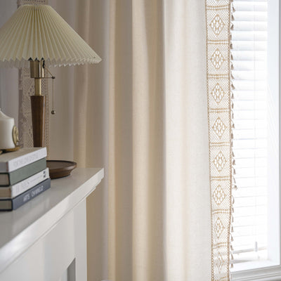 Close-up of a beige semi-transparent curtain with a delicate crochet lace trim and decorative tassels. - Image 3