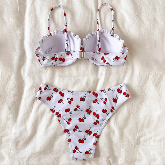 Women's white bikini swimsuit with red cherry print, featuring a ruffled top and high-cut bottom, modeled by a pool. - Image 4