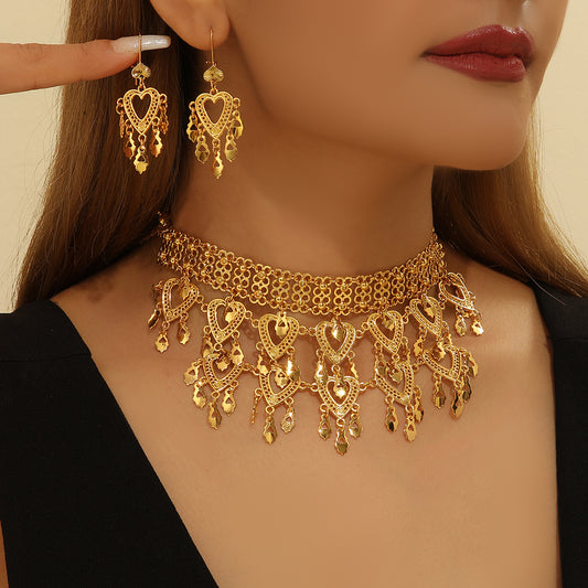 Gold heart-shaped hollow necklace and matching dangle earrings set on a woman wearing a black top.