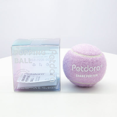 Peach yellow Petdora high elastic tennis ball dog toy next to its clear iridescent 'Popping Ball' packaging. - Image 5