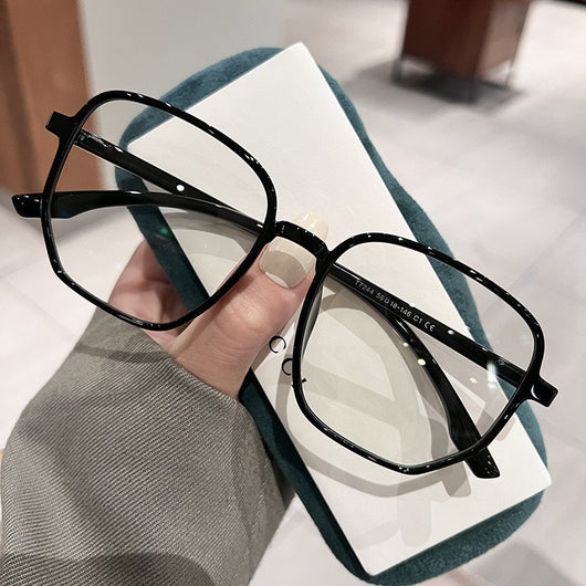 Mocha brown irregular frame glasses with clear lenses, held over a dark green velvet glasses case. - Image 4
