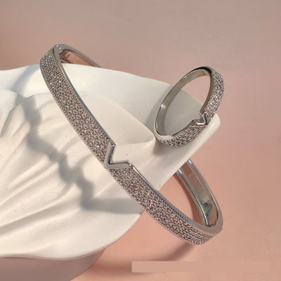 V-shaped 18K gold electroplated bracelet and ring set with pave clear stones on a white stand.