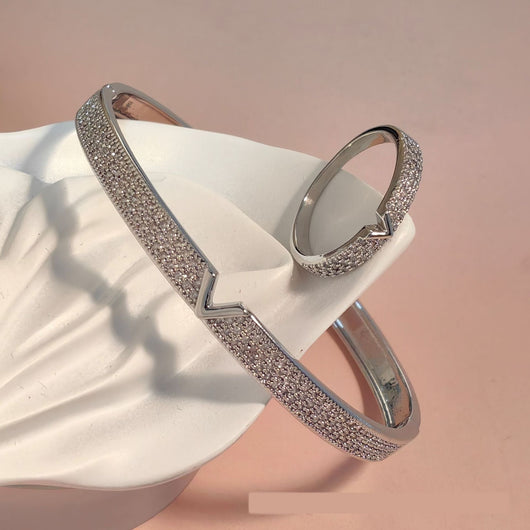 V-shaped 18K gold electroplated bracelet and ring set with pave clear stones on a white stand.