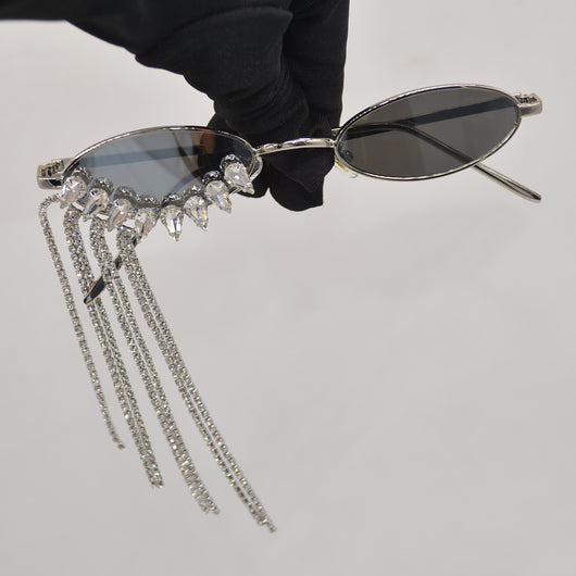 Silver oval-frame sunglasses with mirrored lenses and glamorous rhinestone tassels on one side, held by a gloved hand. - Image 2