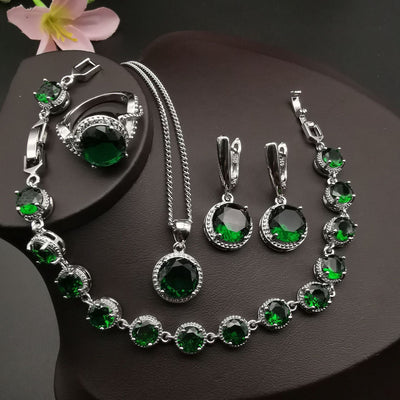 Four-piece silver-tone jewelry set with round green gemstones, including a necklace, bracelet, ring, and dangle earrings.
