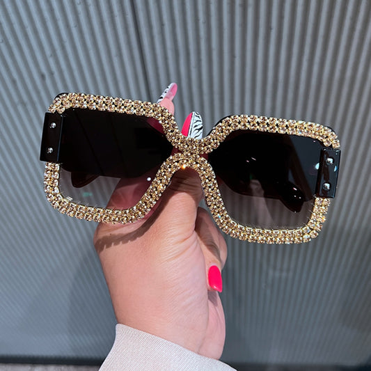 Oversized rectangular sunglasses with black lenses and frames heavily embellished with multiple rows of sparkling rhinestones.
