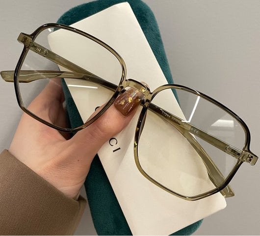 Mocha brown irregular frame glasses with clear lenses, held over a dark green velvet glasses case. - Image 11