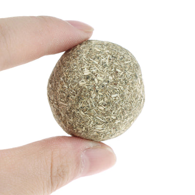 A hand holds a spherical catnip ball made of dried mint leaves and stems, light green and brown in color. - Image 3