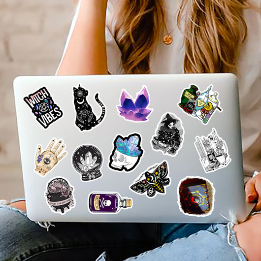 A hand holds a gothic-themed sticker featuring a raven, skull, and crystals, with a pile of 50 assorted waterproof stickers in the background. - Image 17